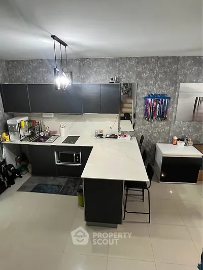 Modern kitchen with sleek black cabinets and white countertops, featuring a built-in microwave and stylish lighting.