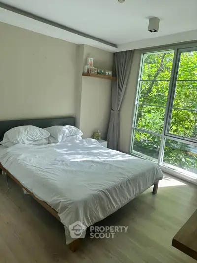 Bright bedroom with large window and modern decor, overlooking lush greenery.