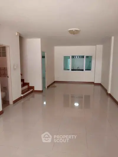 Spacious open-plan living area with tiled flooring and modern kitchen view.