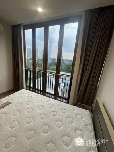 Spacious bedroom with large window offering stunning city view and natural light.