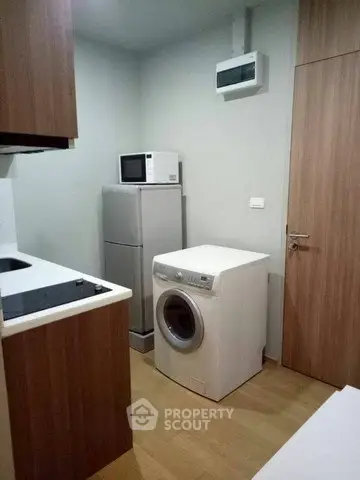 Compact kitchen with washing machine, fridge, and microwave in modern apartment.