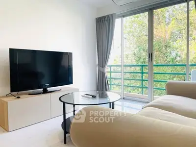 Modern living room with large TV and glass coffee table, bright natural light from balcony.