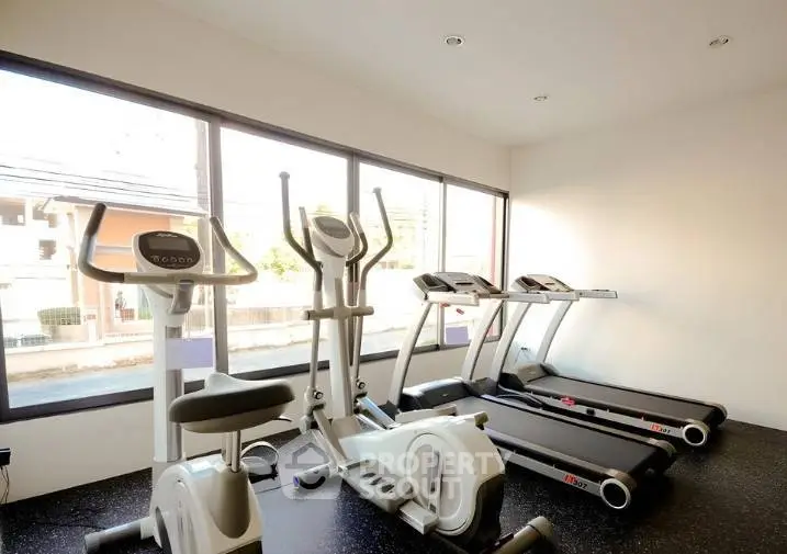 Modern gym with cardio equipment and large windows in a residential building.