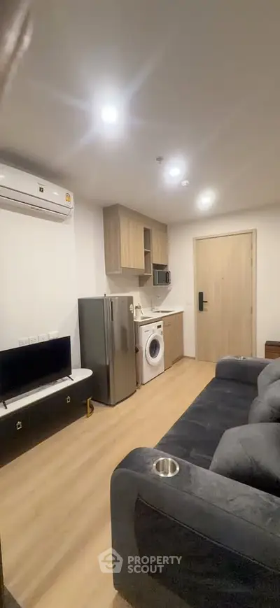 Modern living room with compact kitchen, featuring a washing machine and sleek appliances.