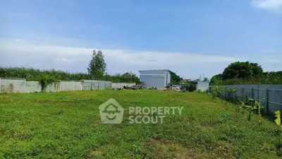 Spacious green plot with potential for development, surrounded by fences and clear blue sky.
