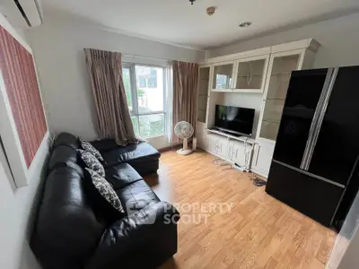 Cozy living room with black leather sofa, TV, and large fridge, perfect for relaxation.