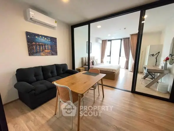 Modern studio apartment with open layout, featuring a cozy living area and stylish bedroom separated by glass doors.