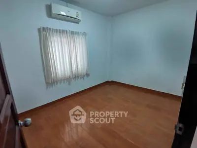 Spacious empty bedroom with wooden flooring and air conditioning unit.