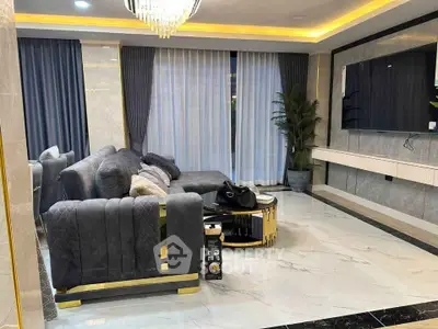 Luxurious modern living room with plush gray sofas, elegant chandelier, and large TV, perfect for relaxation and entertainment.