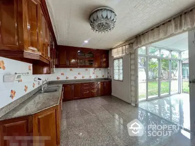 Spacious kitchen with rich wooden cabinetry and gleaming granite countertops, complemented by large windows inviting ample natural light.