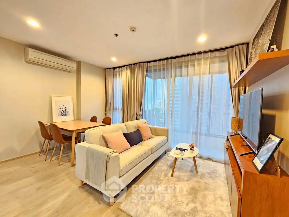 Modern living room with cozy sofa, dining area, and large windows offering city views.