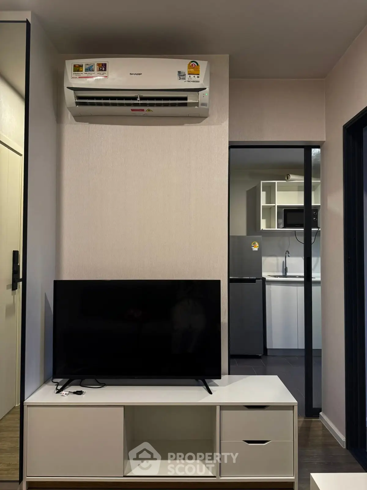 Modern living room with sleek TV setup and air conditioning, leading to a compact kitchen.