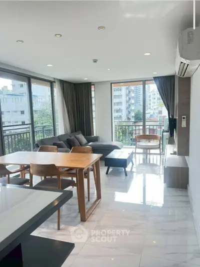 Spacious modern living room with large windows and city view, featuring elegant furniture and natural light.
