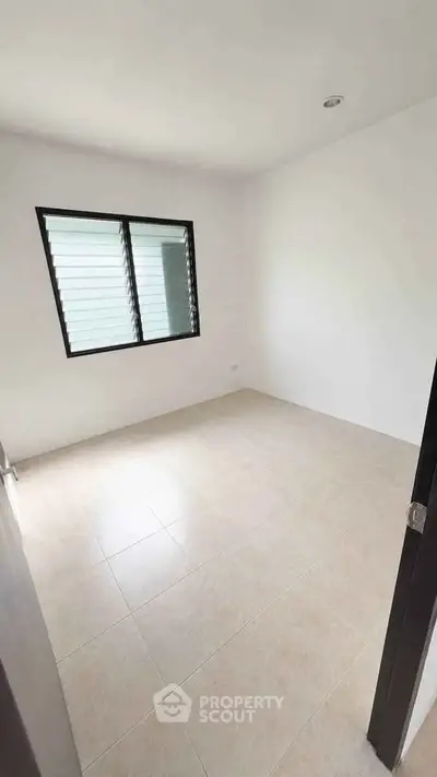 Spacious empty bedroom with tiled floor and large window, perfect for customization.