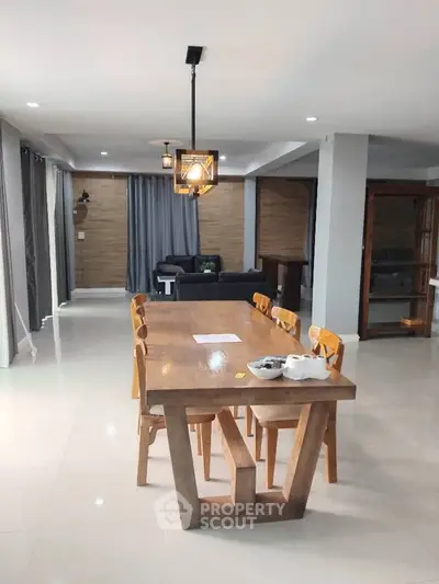 Spacious modern dining area with wooden table and chairs, open layout to living room, elegant lighting.
