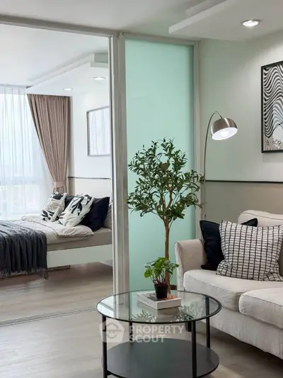 Modern living room with cozy sofa and glass coffee table, leading to a stylish bedroom with natural light.