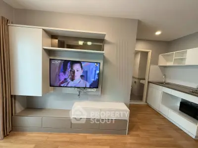 Modern living room with wall-mounted TV and sleek kitchen area in open layout apartment.