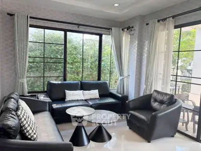 Stylish living room with modern black leather sofas and large windows overlooking greenery.