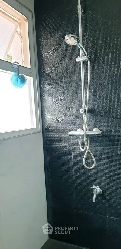 Modern bathroom with sleek black tile shower and window for natural light.