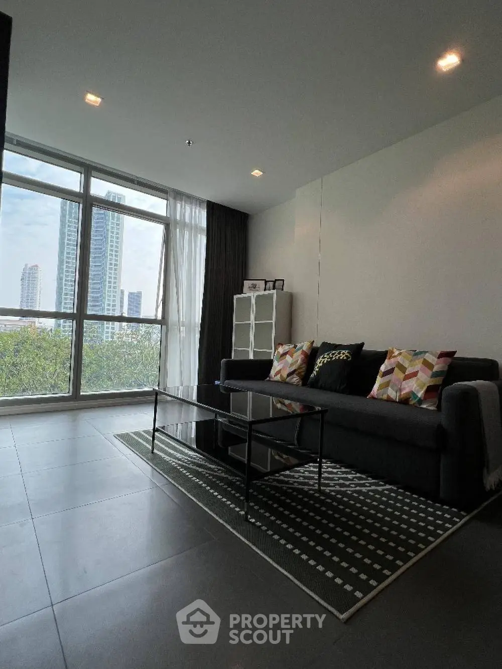 Modern living room with large windows and city view, featuring stylish sofa and decor.