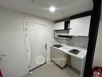 Modern compact kitchen with sleek cabinetry and electric stove in a minimalist apartment.