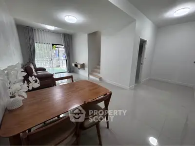 Spacious modern living room with dining area and staircase, featuring sleek furniture and large windows.