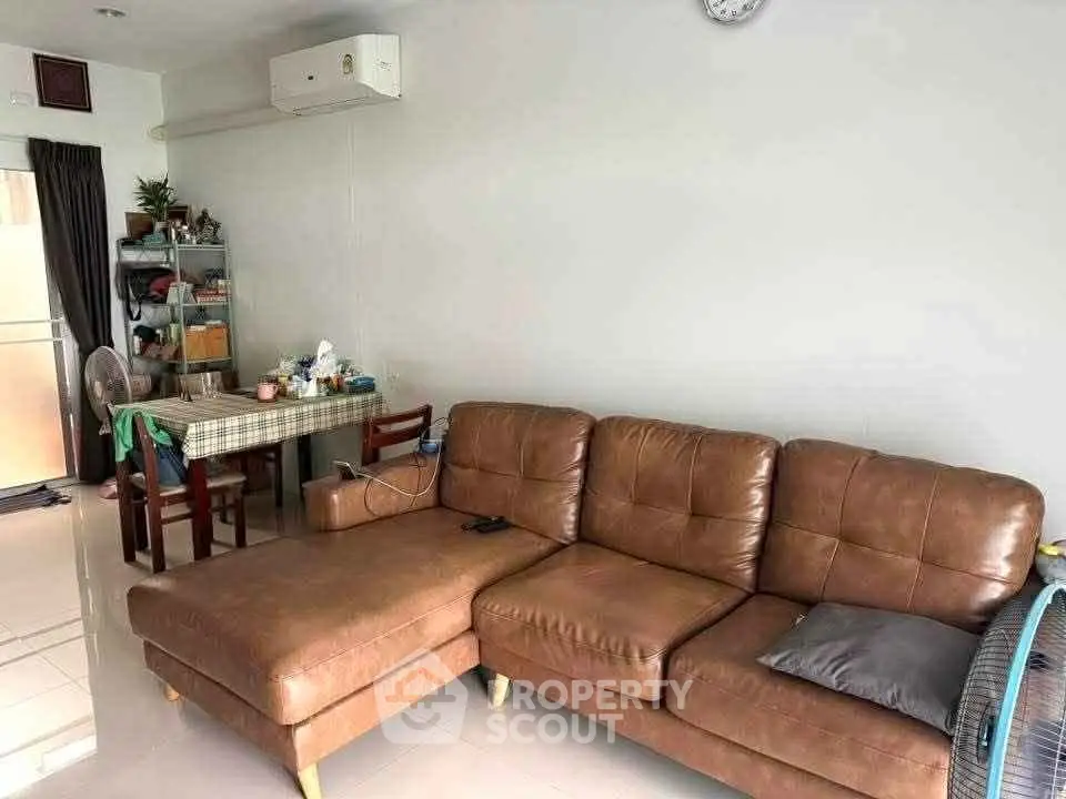 Cozy living room with brown leather sofa and dining area, featuring modern decor and ample natural light.