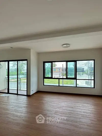 Spacious living room with large windows and balcony access, featuring elegant wooden flooring.