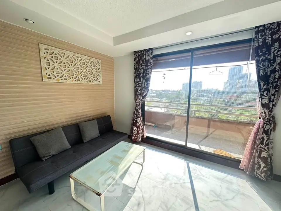 Bright living room with modern sofa and glass coffee table, featuring a large window with city view.