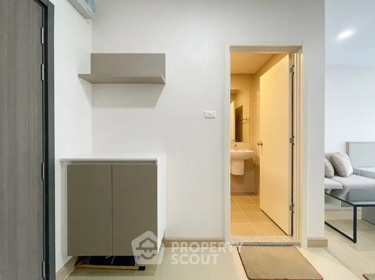 Modern apartment interior with bathroom and living room view, featuring sleek cabinetry and neutral tones.