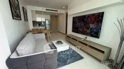 Modern living room with stylish furniture and large TV, open kitchen layout.
