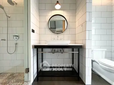 Modern bathroom with sleek vanity and round mirror, featuring a stylish shower area.