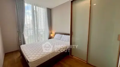 Modern bedroom with large window and city view, featuring a comfortable bed and sleek sliding closet doors.