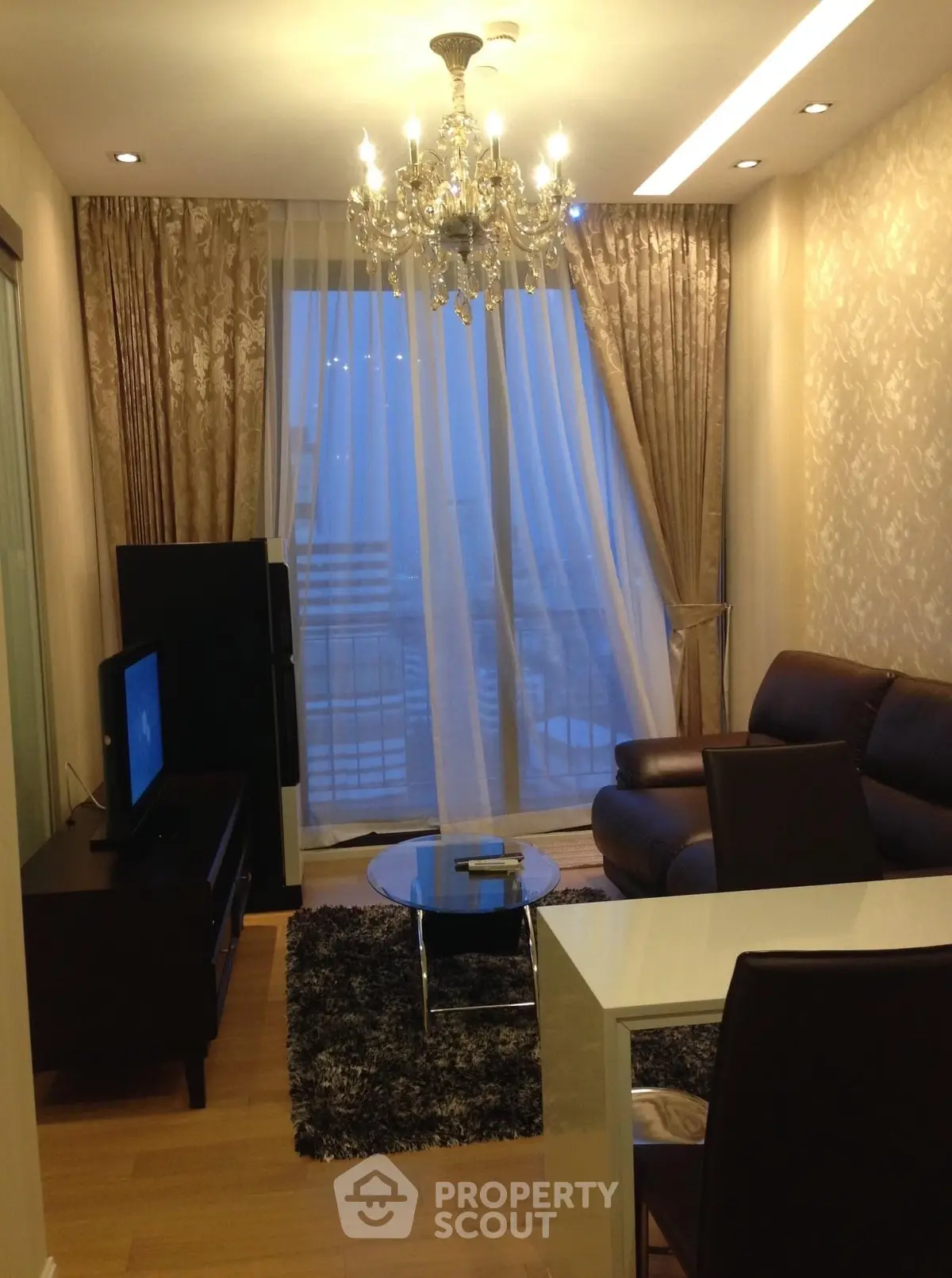 Elegant living room with chandelier, leather sofa, and floor-to-ceiling windows offering a serene view.