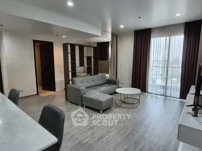 Modern living room with gray sofa, elegant decor, and large windows offering city views.