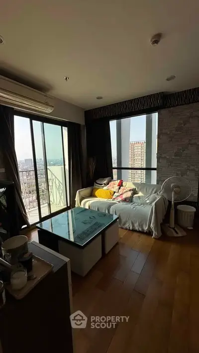 Cozy living room with large windows and city view, featuring a comfortable sofa and modern decor.