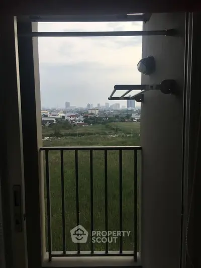 Scenic view from a small balcony overlooking a green field and city skyline.
