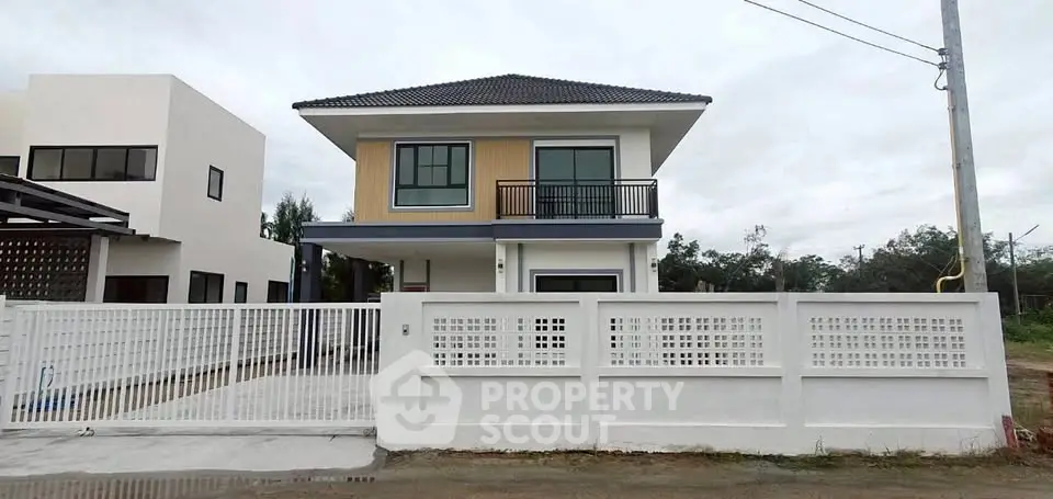 Modern two-story house with balcony and gated driveway in suburban setting.