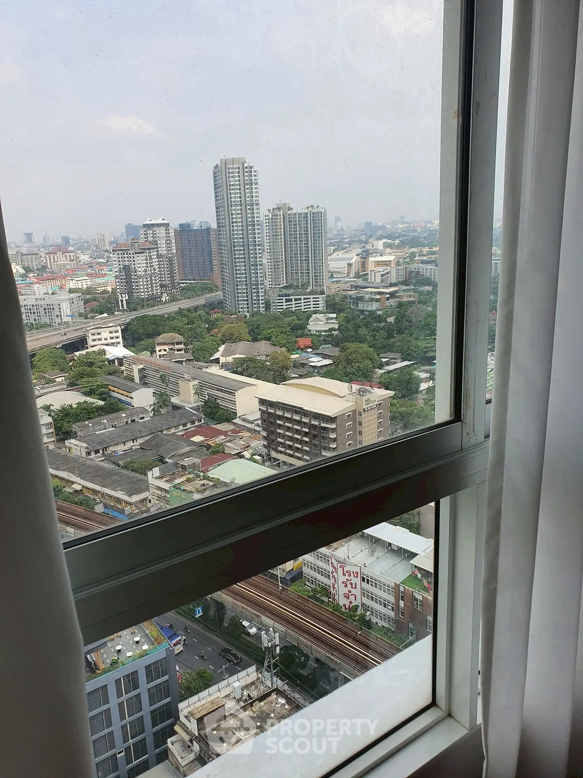 Stunning cityscape view from a high-rise window showcasing urban skyline and lush greenery.