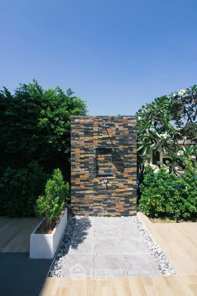 Modern outdoor shower with stone wall and lush greenery