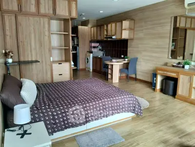 Spacious studio apartment with modern wooden furnishings and integrated kitchen area.