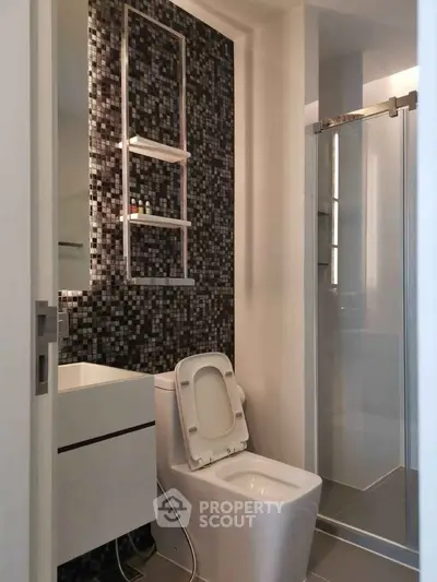 Modern bathroom with sleek design, featuring a glass shower and mosaic tile accent wall.