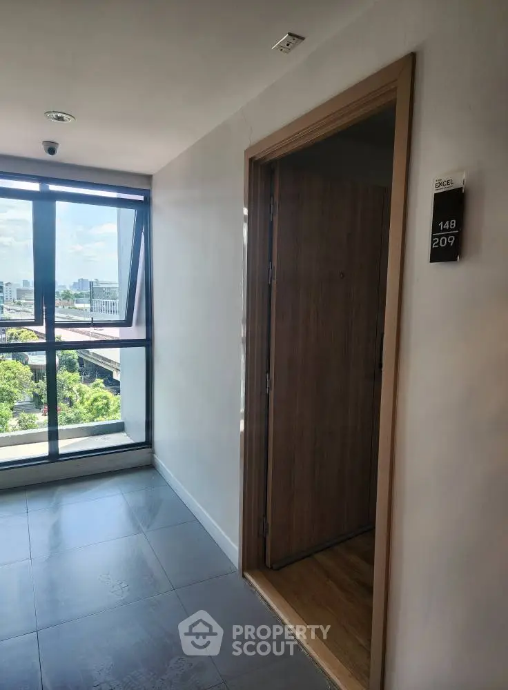 Modern apartment hallway with open door and city view through large window.
