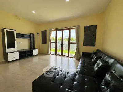 Spacious living room with modern black leather sofas and large windows offering natural light.