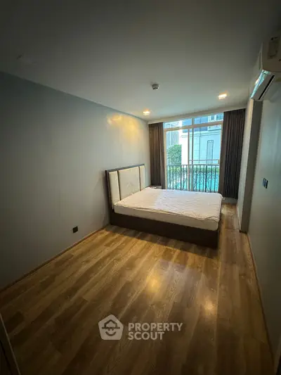 Spacious bedroom with wooden flooring and large window overlooking greenery.
