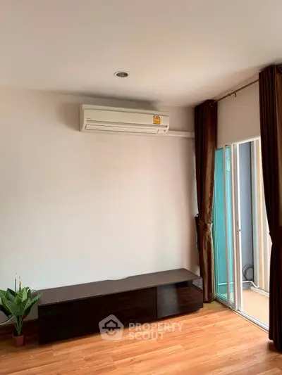 Modern living room with air conditioning and wooden flooring, featuring a sleek TV stand and balcony access.