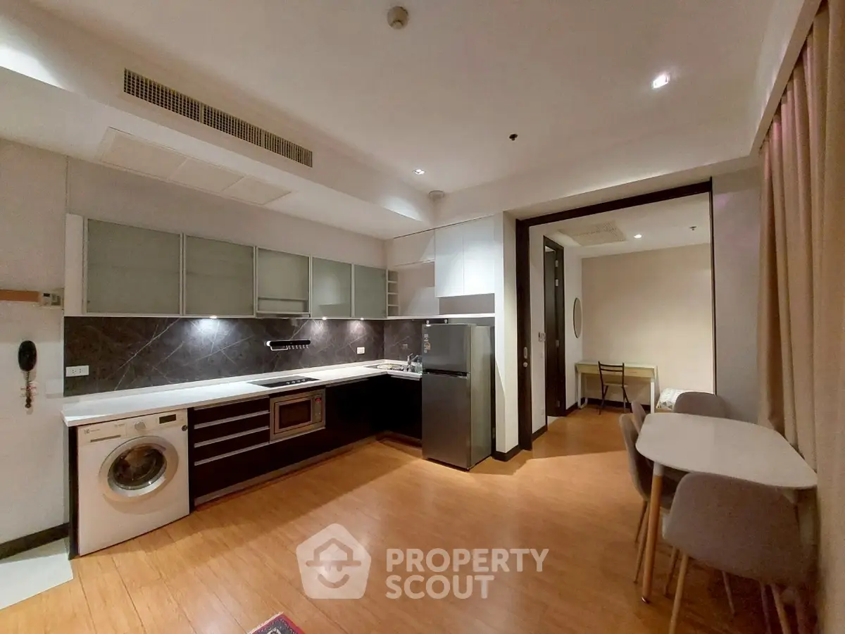 Modern kitchen with open layout and dining area, featuring washing machine and sleek appliances.