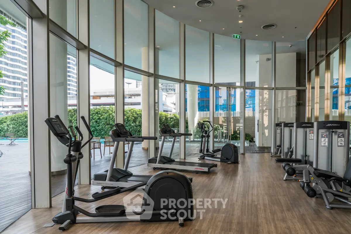 Modern gym with state-of-the-art equipment and floor-to-ceiling windows offering a pool view.