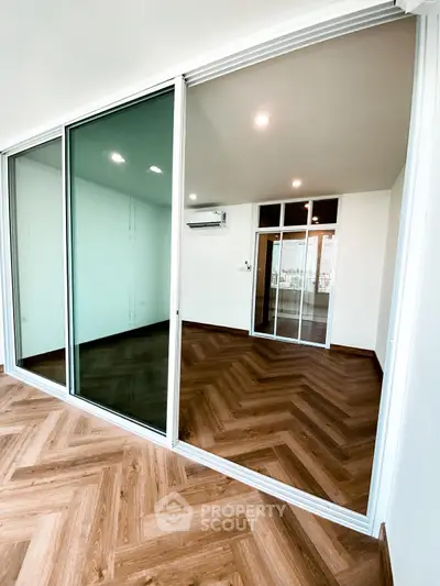 Spacious modern room with wooden flooring and large glass sliding doors, perfect for versatile living space.
