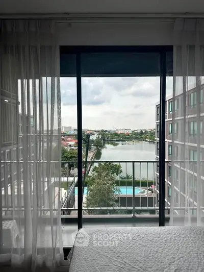 Stunning bedroom view with floor-to-ceiling windows overlooking a serene lake and modern apartment complex.